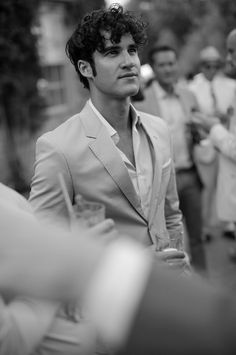 two pictures of a man in a suit and tie with other men standing around behind him