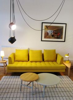 a living room with a yellow couch and two lamps hanging from the ceiling above it