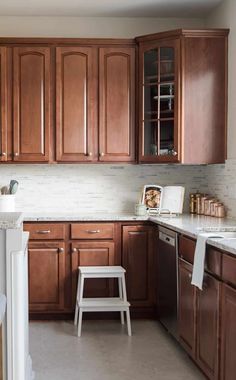 a kitchen with wooden cabinets and white counter tops, two stools in the middle