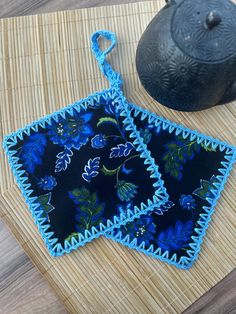 two blue crocheted pot holders sitting on top of a bamboo mat next to a teapot