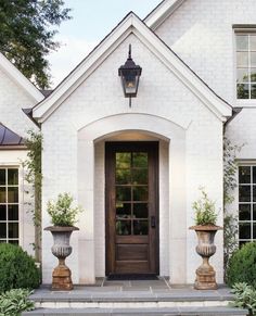 a white house with two large planters in front of it and a brown door