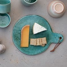 cheese and crackers are on a plate next to cups, mugs and seashells