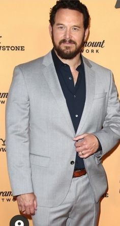 a man in a gray suit and black shirt is standing on the red carpet with his hands in his pockets