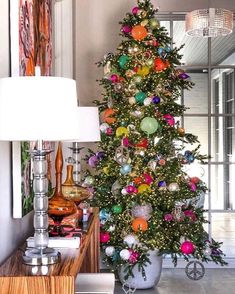 a brightly colored christmas tree in a living room next to a lamp and painting on the wall