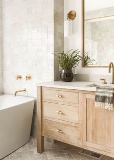 a white bath tub sitting next to a wooden sink vanity in a bathroom under a mirror