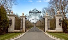 a gated driveway leading to a large house with trees and bushes on both sides