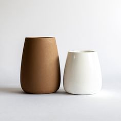 two white and brown vases sitting next to each other on a white table top