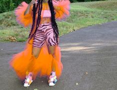 a woman with long braids standing in the middle of a road wearing an orange and pink outfit