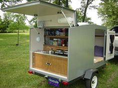 an outdoor kitchen is built into the back of a trailer with its door open and shelves on it