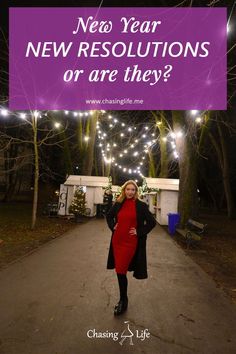 a woman in a red dress is standing on a path with christmas lights behind her