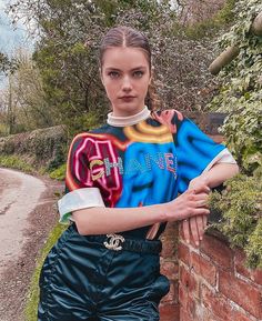 a woman leaning against a brick wall with her hands on her hips and looking at the camera