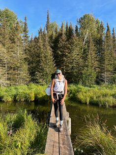 a woman is sitting on a wooden bridge over a river with trees in the background