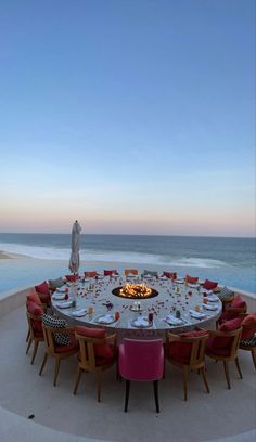 an outdoor dining area overlooking the ocean at sunset with fire pit and table set for six