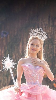 a woman in a pink dress holding a wand and wearing a tiara on top of her head