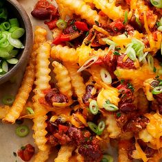 a plate filled with cheesy fries and some green onions on the side next to a bowl