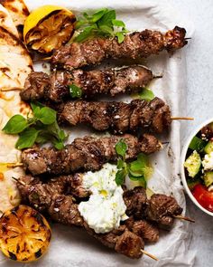 grilled meat and vegetables on skewers next to a bowl of feta