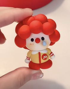 a close up of a person holding a small toy with red hair and a clown face