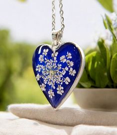 a blue heart shaped pendant with white flowers on it sitting next to a potted plant