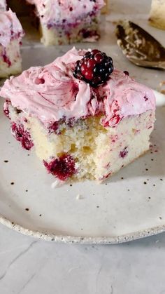 a piece of cake with pink frosting and berries on top is sitting on a plate