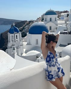 a woman in a blue and white dress leaning against a wall on top of a building