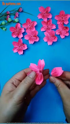 someone is making pink paper flowers on a blue surface with green stems and small white flowers