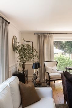 a living room filled with furniture and a large window covered in curtains next to a wooden floor