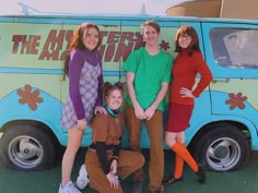 four people are posing in front of a van with the words the mystery machine on it