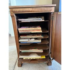 a wooden cabinet filled with lots of books on top of carpeted floor next to a wall