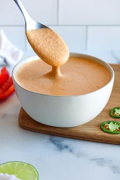 a spoon full of sauce being held over a bowl filled with guacamole