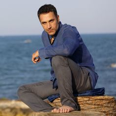 a man sitting on top of a tree stump next to the ocean with his hand on his hip