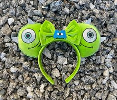 a green headband with two eyes and a bow on top of some rocks in the ground