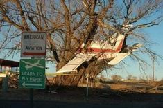 an airplane that is sitting in the air next to a road sign and some trees