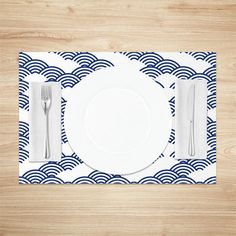 a place setting with blue and white waves on the table cloth, silverware and utensils