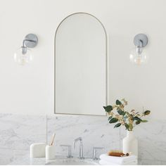 a bathroom with marble counter tops and white walls, along with an oval mirror on the wall