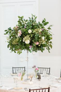 a tall centerpiece with flowers and greenery sits on top of a round table