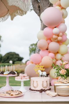 a table topped with cakes and desserts next to a tall tree filled with balloons