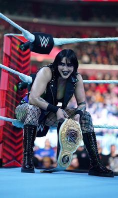 a woman in fishnet stockings and boots holding a wrestling belt, kneeling on the ground