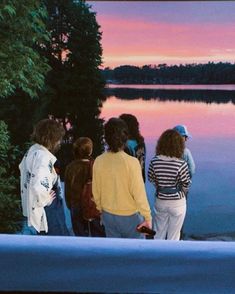 group of people standing on the edge of a lake at sunset looking out to sea