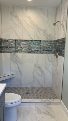 a bathroom with white marble tile and gray tiling on the shower wall, toilet and sink