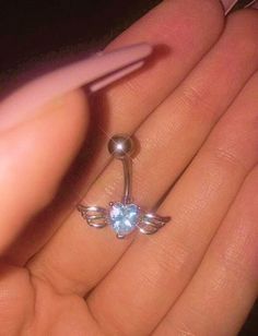 a person's hand holding an upside down nose ring with wings and a light blue topaz