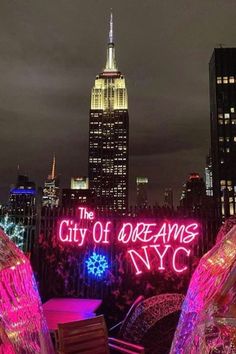 the city of dreams nyc sign is lit up in pink and purple lights, with skyscrapers in the background