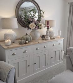 a white dresser topped with lots of vases filled with flowers next to a mirror