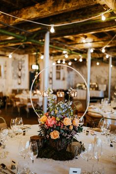 an arrangement of flowers and greenery is displayed in the center of a round table