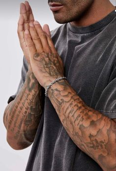 a man with tattoos on his arm and wrist is holding his hands together in prayer