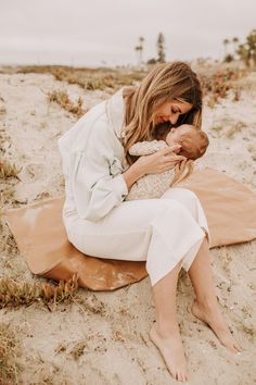 a woman sitting on the beach holding a baby