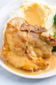 a white plate topped with meat and gravy covered in gravy next to broccoli