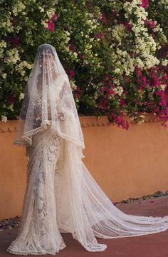 a woman in a wedding dress with a veil on her head and flowers behind her