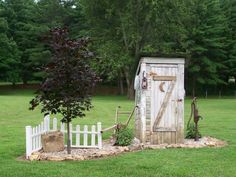 an outhouse in the middle of a field with a tree and fence around it