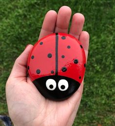 a hand holding a rock with a ladybug painted on it's face