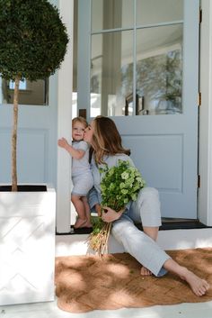 a woman holding a baby and kissing her on the cheek while sitting in front of a door